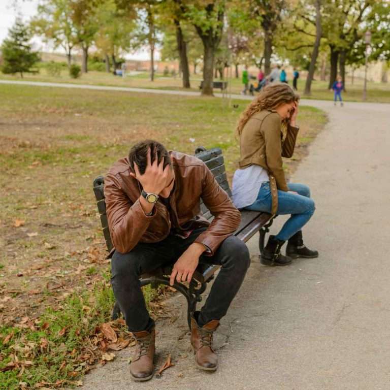 Pareja sentada en un banco, distanciada y enfadada, representando el final de una relación y el proceso de dejar de idealizar a un ex.
